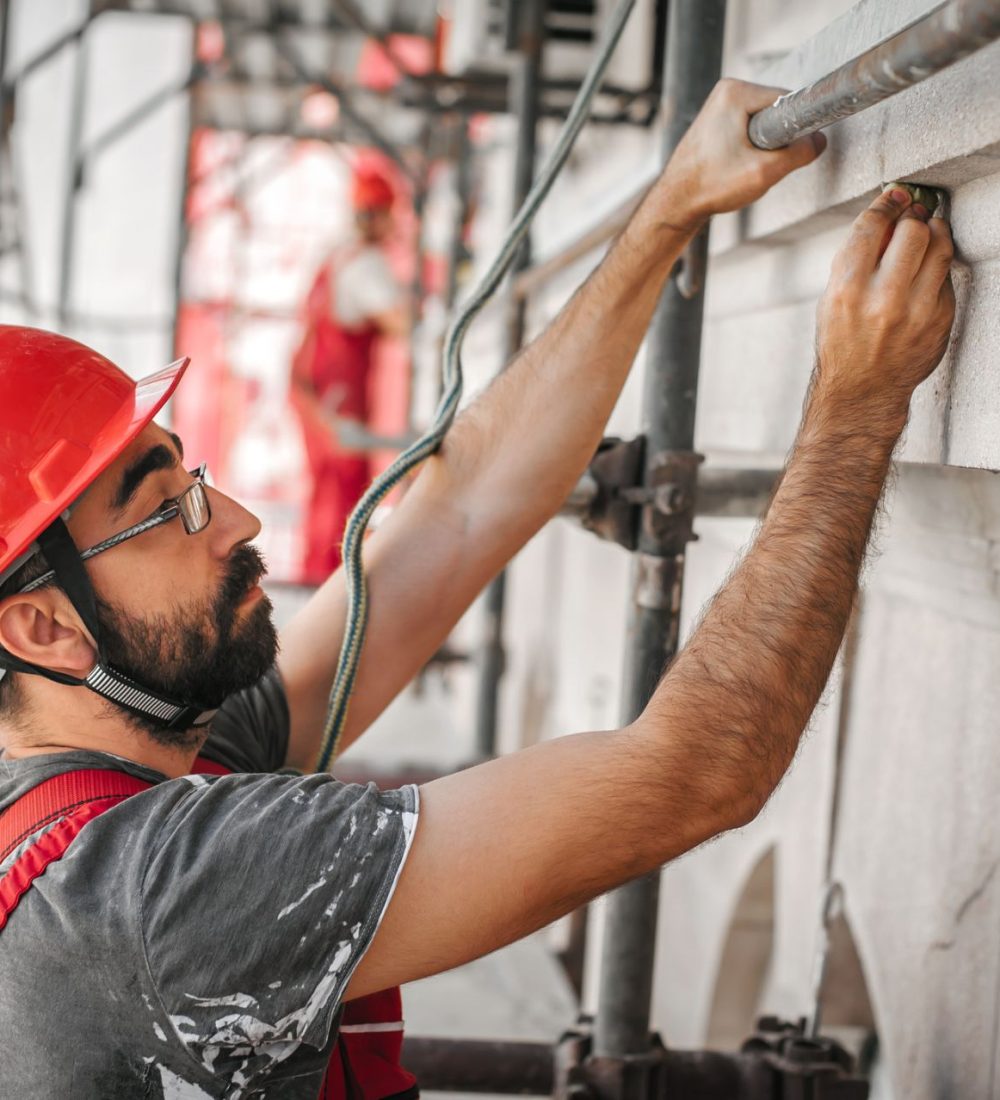 Man worker standing on scaffolding, perform work on the restoration of the facade of the old building. Repairing and renovate